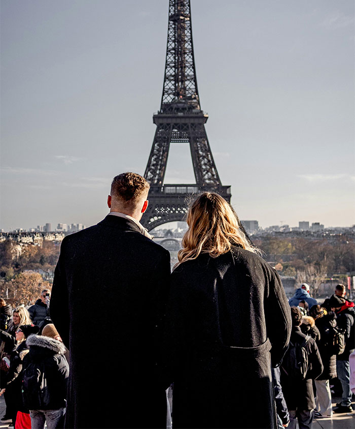 Couple standing near Eiffel Tower, where guy offers GF a fake proposal in Paris among tourists. Couple standing near Eiffel Tower, where guy offers GF a fake proposal in Paris among tourists.