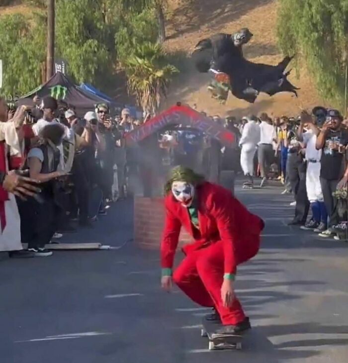 Person in a Joker costume skateboarding down a crowded street with a gorilla costume in the background.