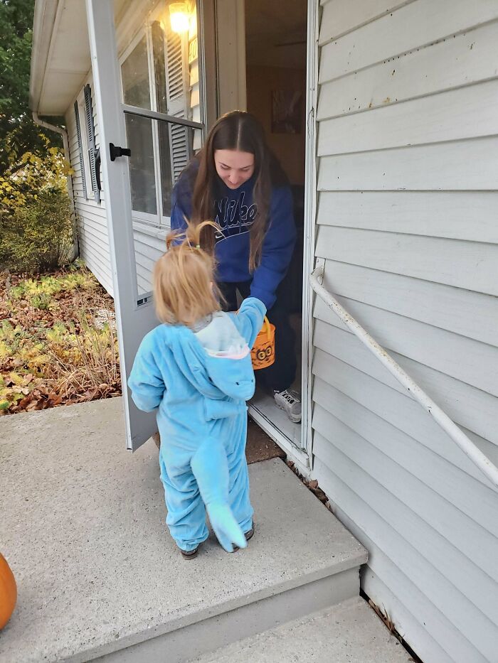 Toddler in blue costume trick-or-treating at front door, capturing wholesome and funny dads doing their best moments.