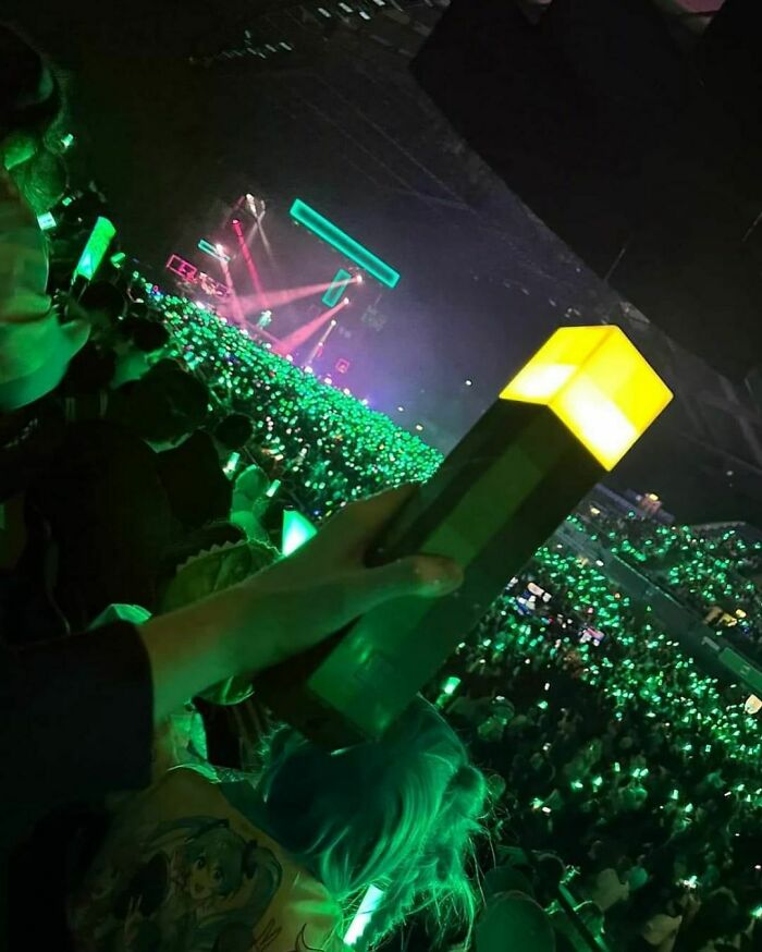 Concert crowd holding glowing lights, creating a vibrant sea of green, showcasing "Pics That Go Hard" energy.