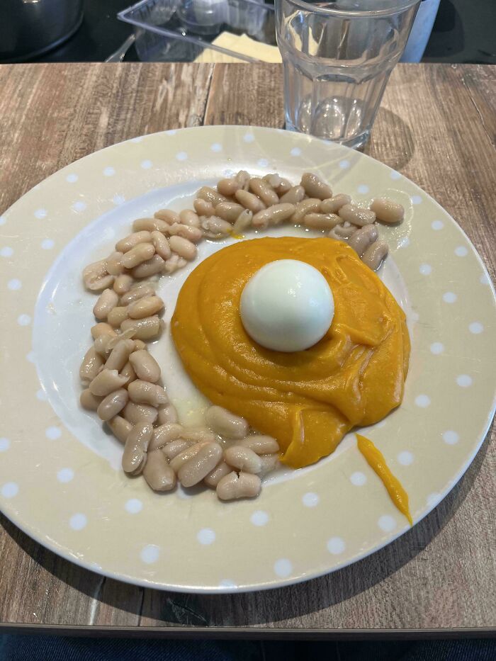 A bizarre dish featuring beans, mashed orange puree, and a whole egg on a polka dot plate.