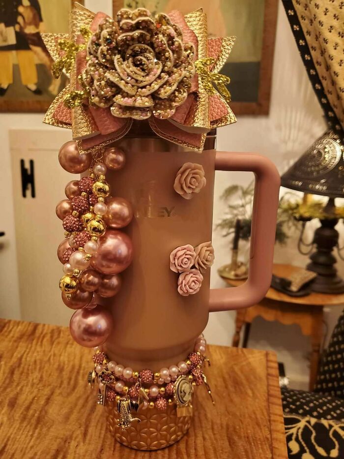 Overdecorated tumbler with floral and pearl embellishments, representing a critique of consumerism.