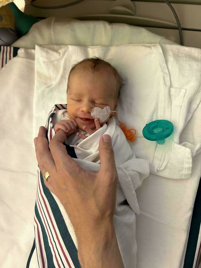 Padre sosteniendo con ternura a su bebé recién nacido en hospital, capturando momentos de crianza amorosa y divertida.