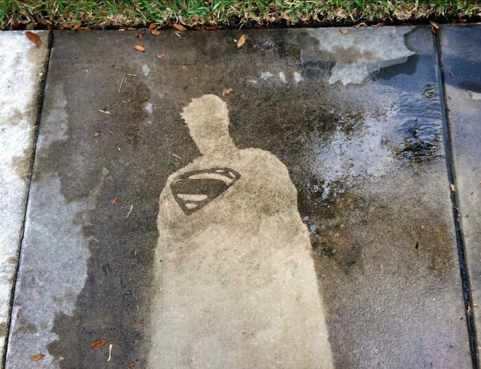 Superman silhouette revealed on a dirty sidewalk after power washing, showcasing satisfying cleaning results.