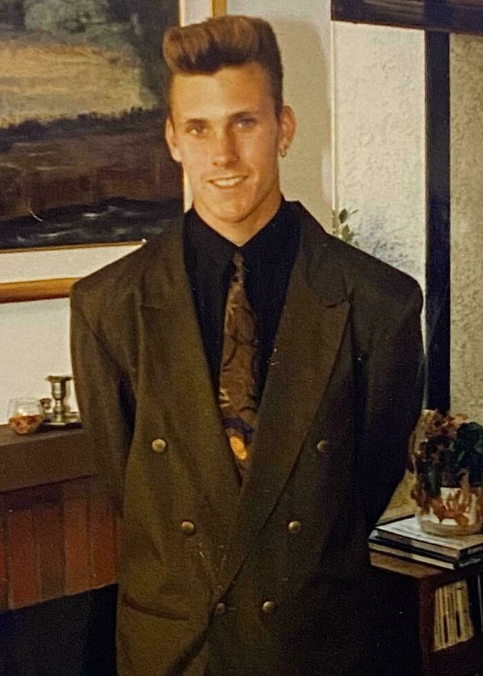 Man in an oversized suit with a high hairstyle, embodying blunder years fashion in a vintage living room setting.