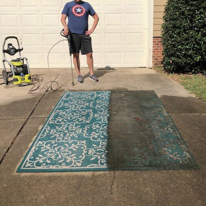 A person power washing a dirty rug, revealing a clean, vibrant pattern on the driveway.