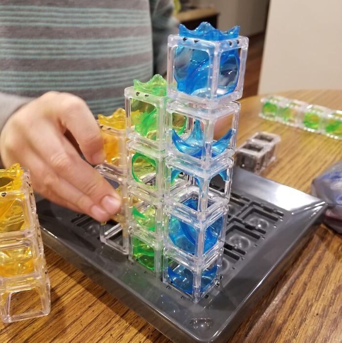 A child’s hand stacking colorful translucent puzzle pieces, a fun gift idea for shopping for a 12-year-old.
