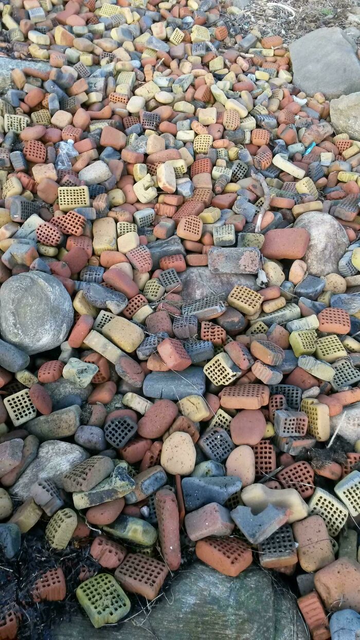 Colorful terra cotta pieces and rocks, quirky treasures washed ashore, piled together on a beach.
