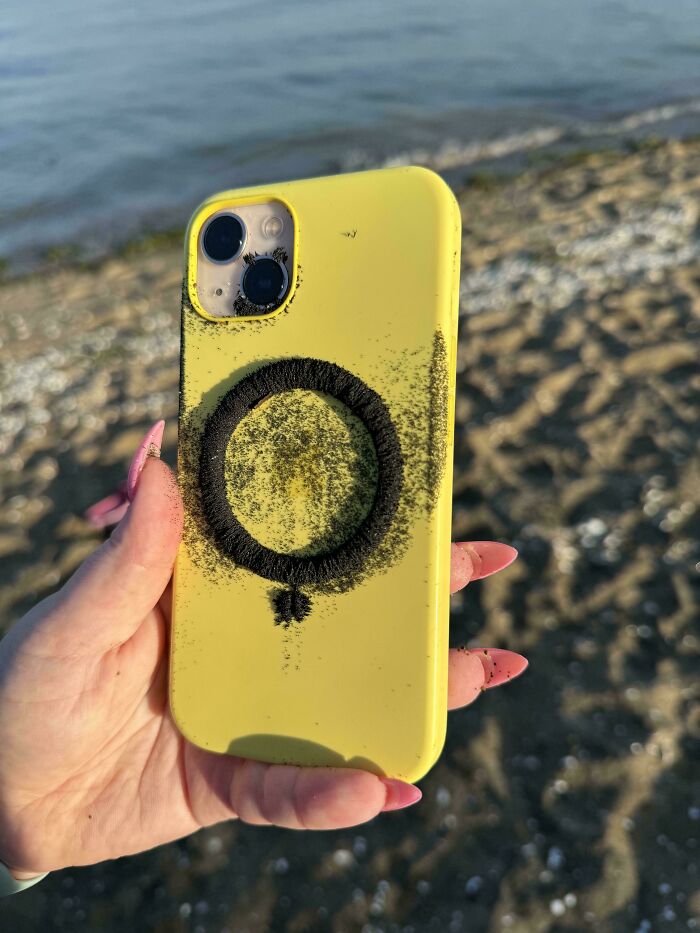 Yellow phone case with sand pattern, quirky treasure found washed ashore, held by a person with pink nails at the beach.