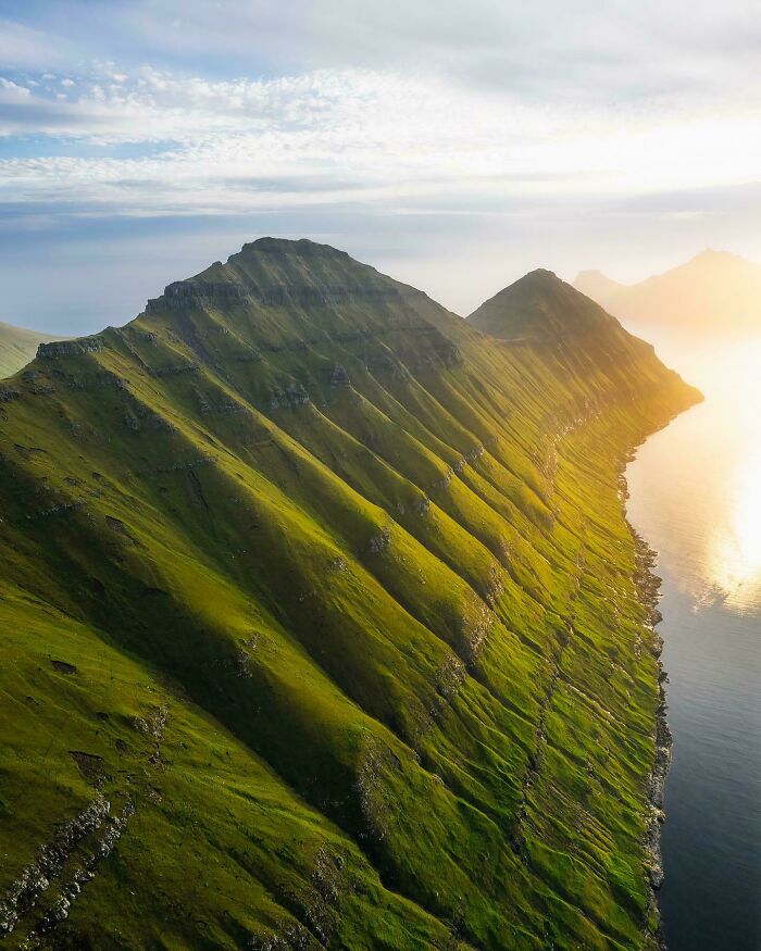 Green mountain ridge at sunrise, highlighting nature's beauty next to calm waters.