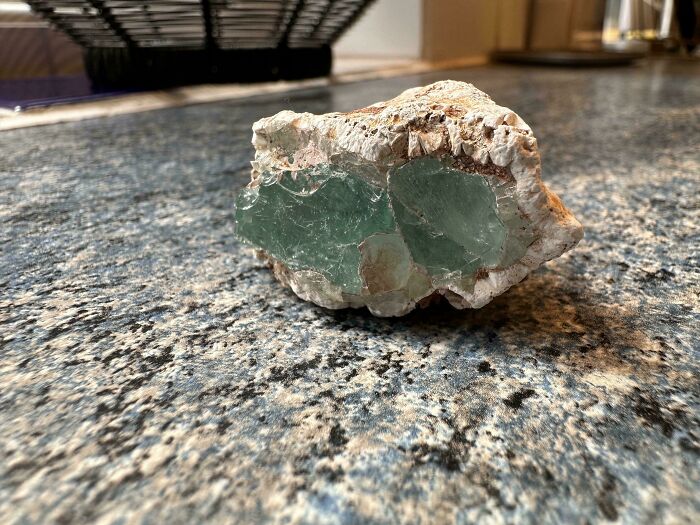 Quirky treasure found washed ashore: a green crystal embedded in a rocky surface on a speckled countertop.