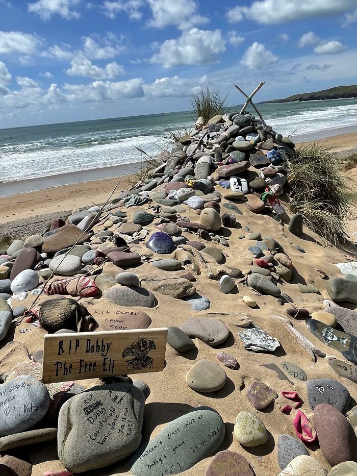 Quirky treasure: beach tribute with stones and a sign for Dobby, adorned with messages and seashells.