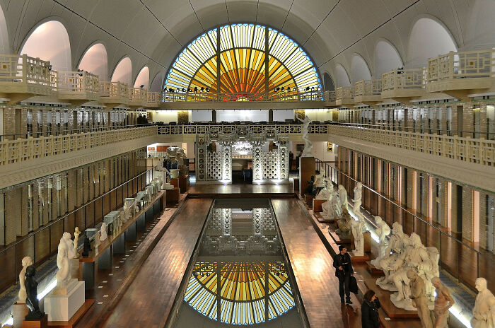 Art museum in a converted building with sculptures and a stained glass window, showcasing stunning building conversions.