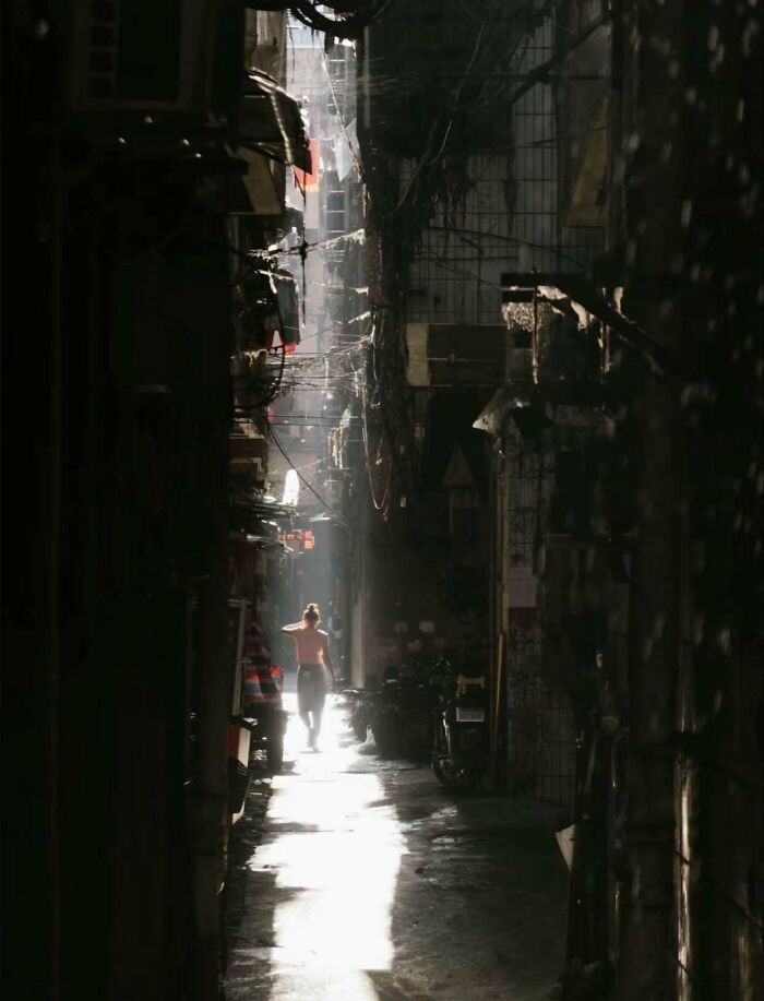 Narrow, dimly lit urban alley with a person walking, highlighting urban hell conditions.