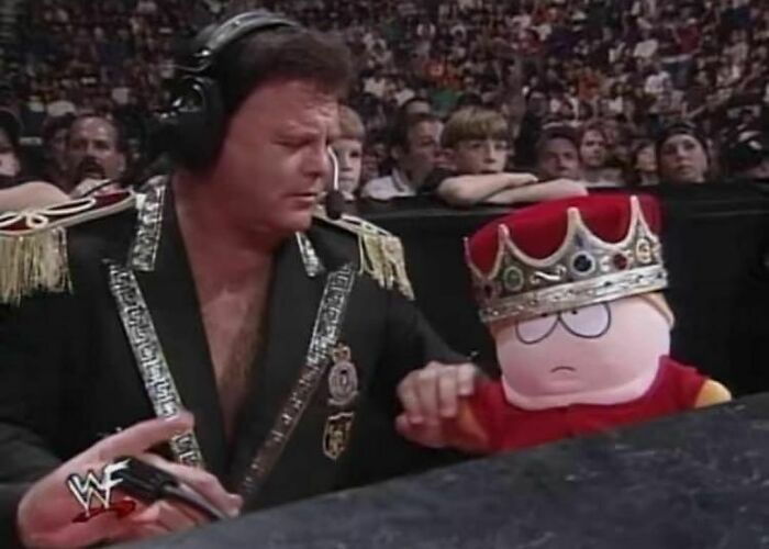 A man in regal attire with a plush toy wearing a crown at a wrestling event, embodying "pics that go hard" vibes.