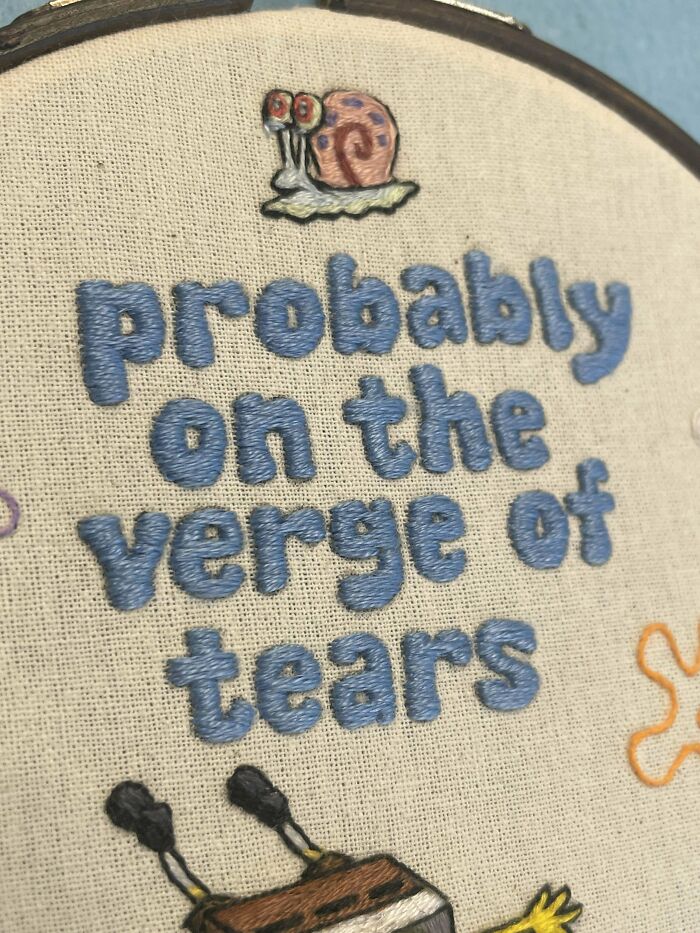 Close-up of embroidery design with blue stitched text and small colorful stitched snail on fabric.