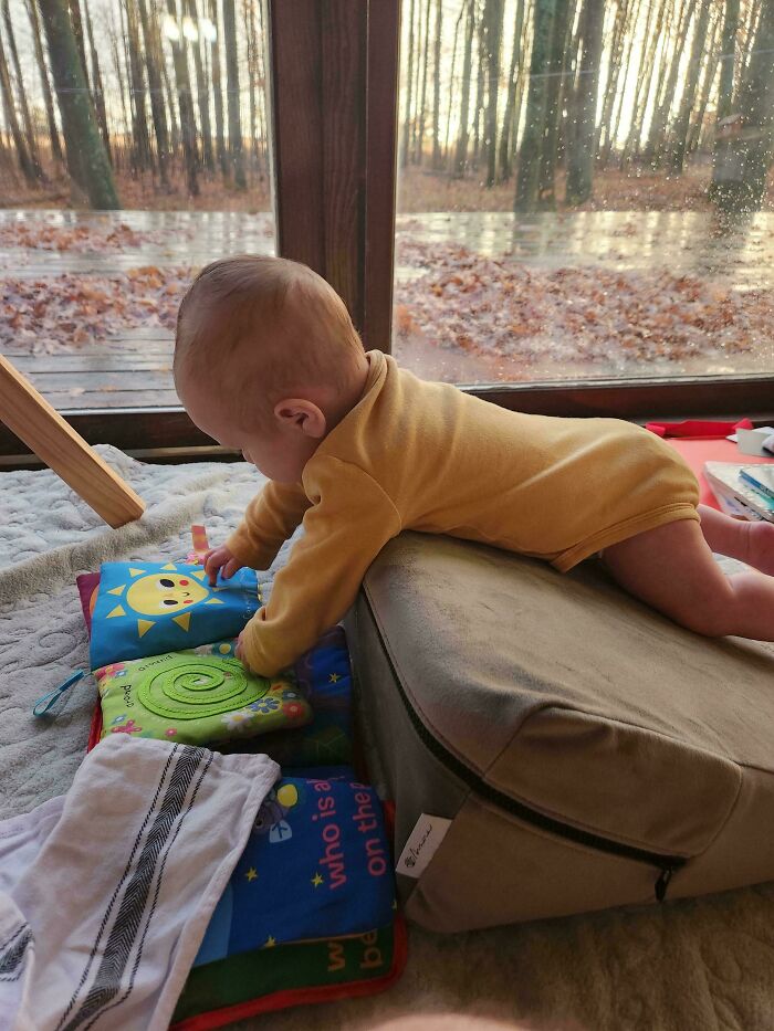 Baby playing on a cushion and colorful soft books inside a cozy home, showcasing wholesome and funny dads moments.