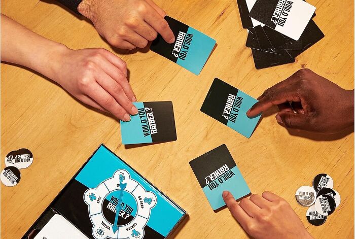 Hands holding and playing cards from a compact and straightforward game on a wooden table with game pieces visible.