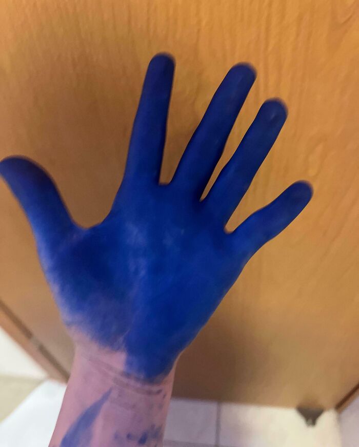 Blue-stained hand after hair dye mishap, illustrating hair-cutting-dyeing-fails indoors against a wooden background.