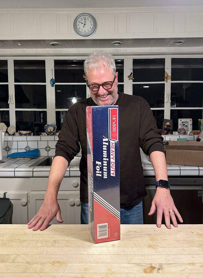 Man laughing at a comically large box of aluminum foil in a kitchen; online shopping fail.
