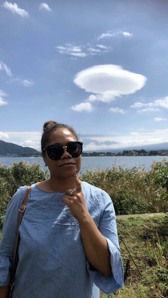 Woman in sunglasses pointing at unique cloud shape above a lake, a fascinating sky phenomenon.