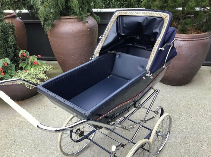 Vintage pram found while thrifting, featuring a dark blue interior and chrome frame, positioned outdoors near large planters.