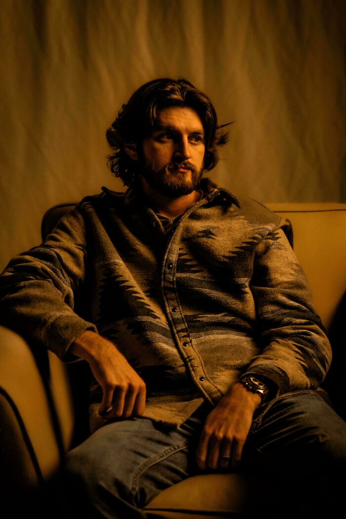 Man in warm lighting sitting on a couch, resembling a Renaissance painting.