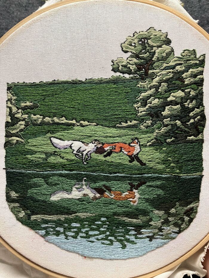 Embroidery design of two foxes playing near a pond with trees, showcasing detailed and beautiful embroidery artwork.