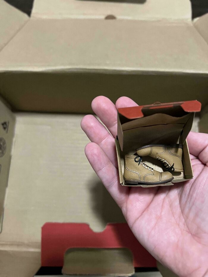 Hand holding tiny boots in a box, showcasing online shopping fail.