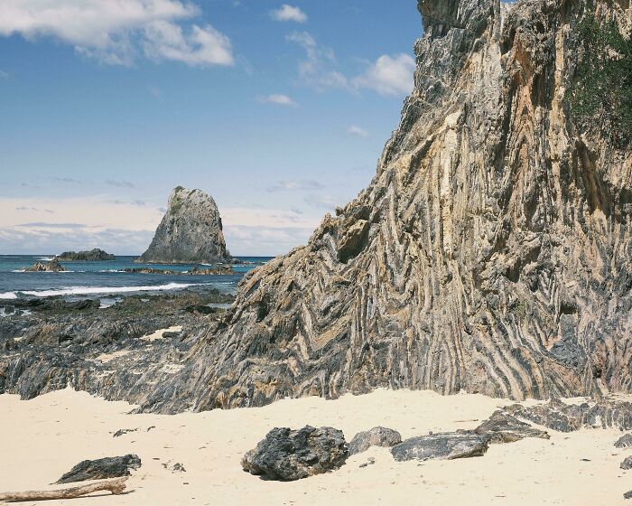Rocky beach landscape with unique, wavy rock formations and distant island under a blue sky; quirky treasures of nature.