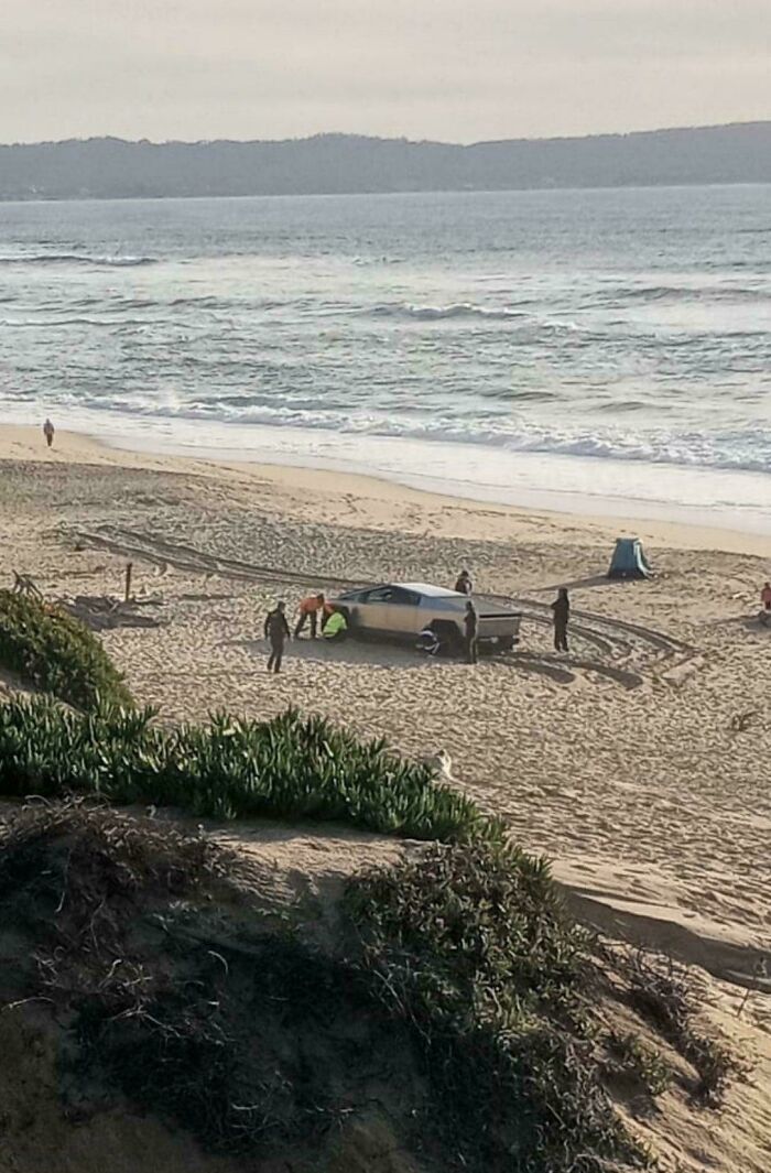 Car stuck in sand on beach as people gather around, illustrating regret after spending money.