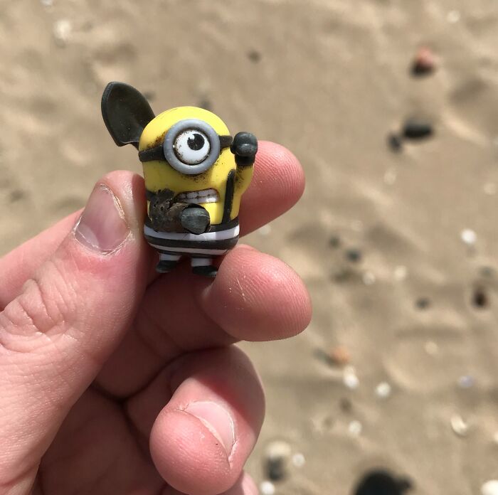 A quirky treasure washed ashore: a small toy figure held on a sandy beach.