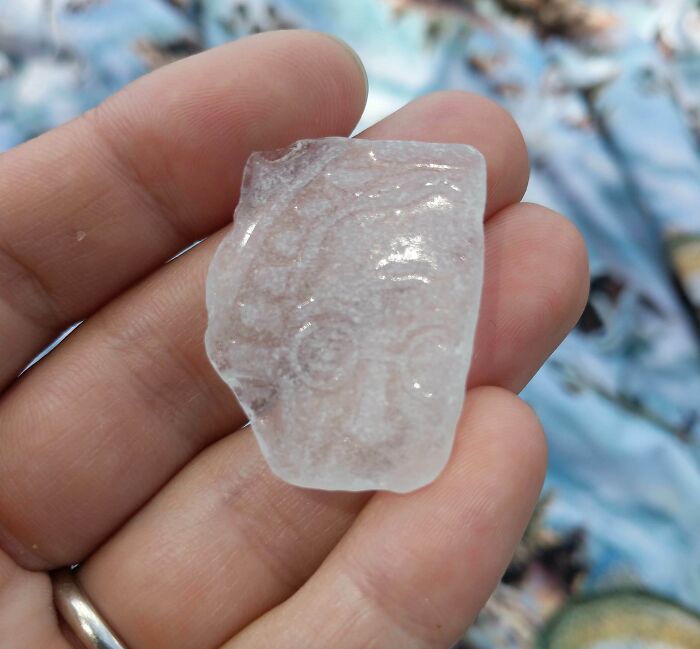 Quirky treasure found ashore: a translucent stone with an etched face in a person's hand.