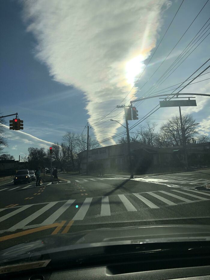 Fascinating cloud shape resembling a column of light over a street intersection with traffic lights and cars.