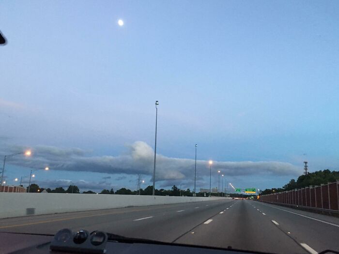 Highway view with fascinating cloud shapes resembling a creature, under a twilight sky and visible moon.