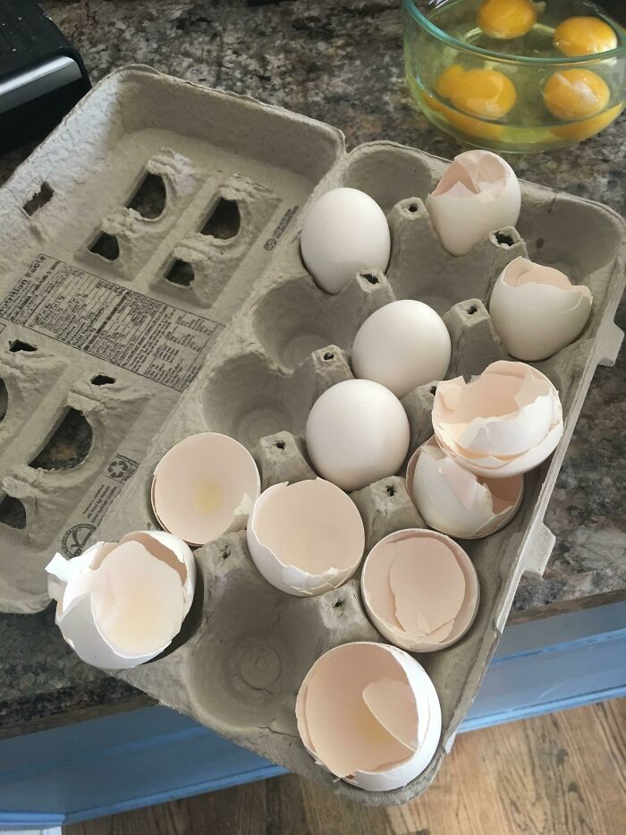Empty cardboard egg carton with broken eggshells, yolks in a bowl on the counter, capturing infuriating girlfriends moment.