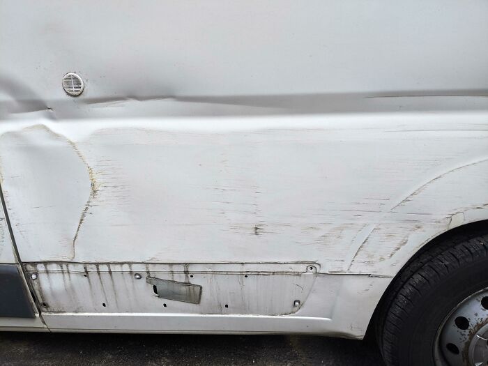Damaged white van with dents and scratches, showing regretful spending decision.