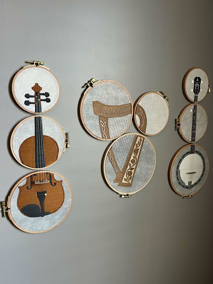 Embroidery designs of musical instruments displayed in wooden hoops hanging on a gray wall for decoration.