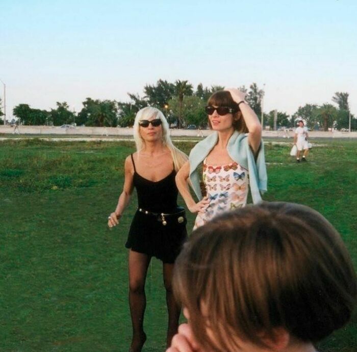 Two women in '90s fashion wearing sunglasses in a park, capturing a nostalgic moment.