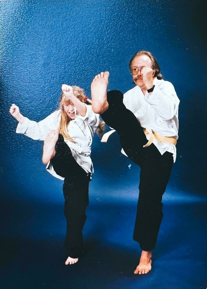 Two people in martial arts poses wearing white uniforms, kicking high during their blunder years in a studio setting.