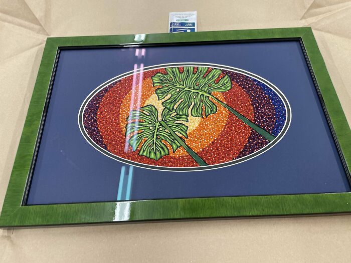 Framed embroidery design featuring green leaves with vibrant orange and red background in an oval pattern.