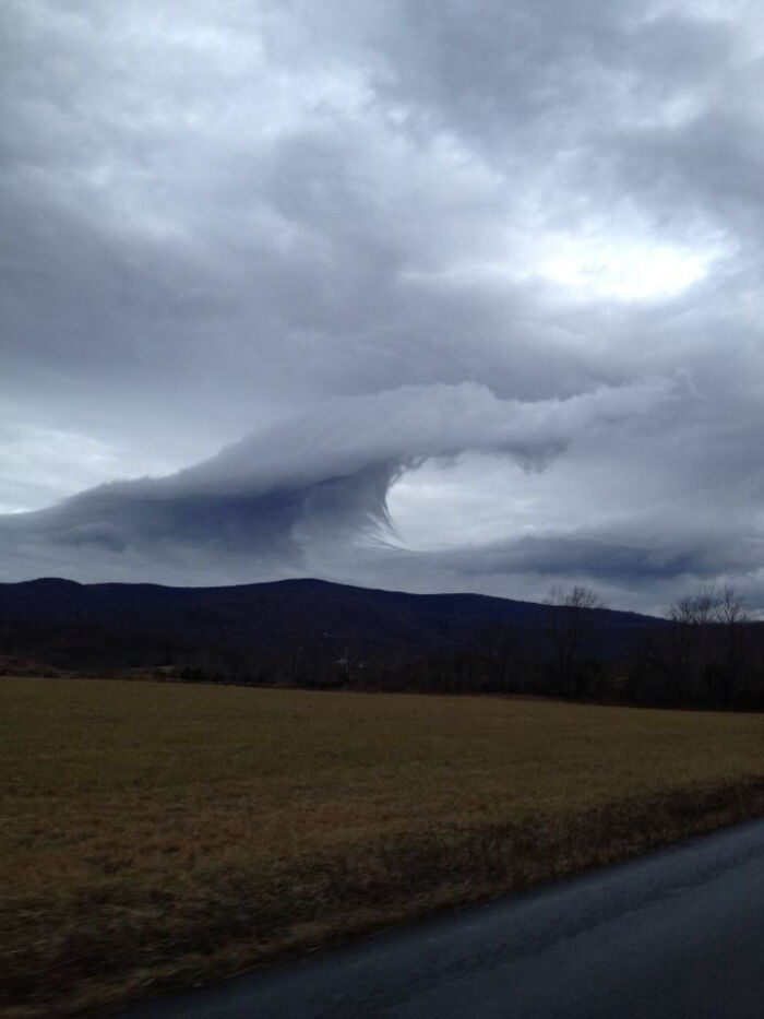 Fascinating cloud shape over a mountainous landscape, resembling a swirling vortex under a moody sky.