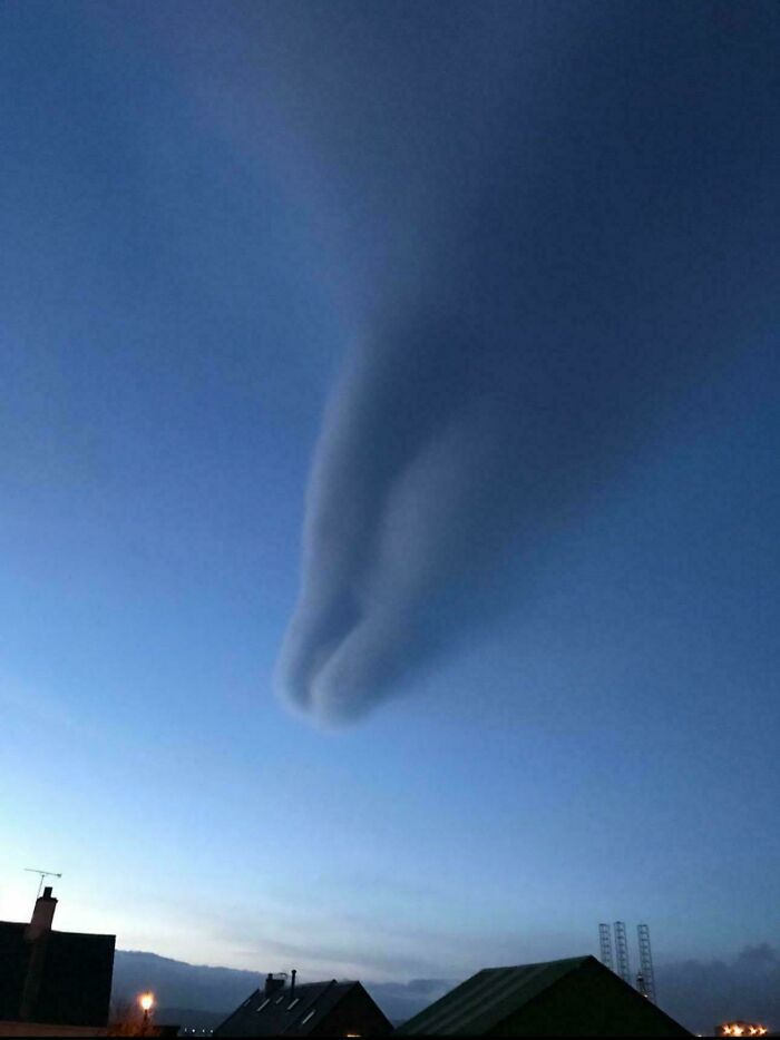 Unusual cloud shape resembling a hand against a twilight sky over rooftops.