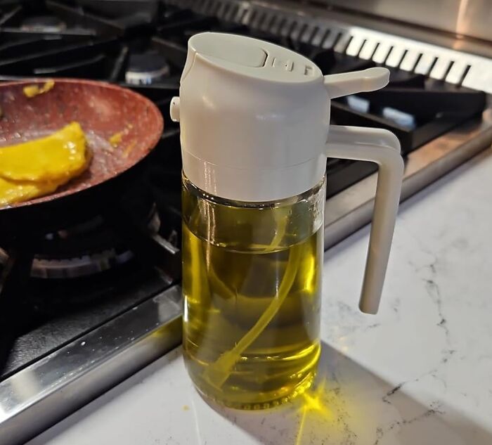Clear oil dispenser with white lid and handle on kitchen counter near stove with frying pan cooking food, popular Amazon find.