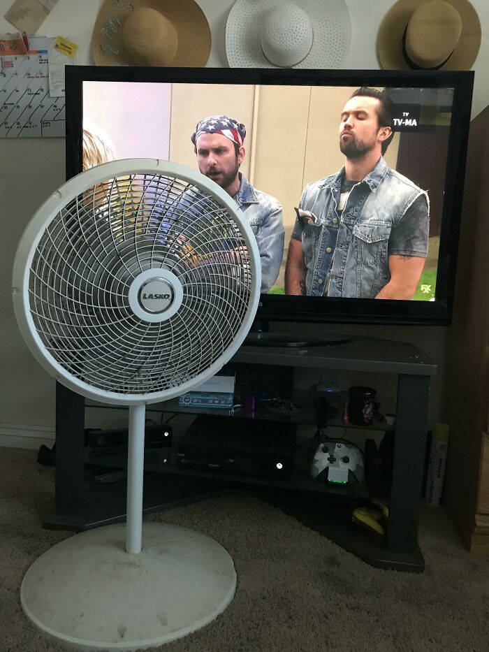 A fan blocking the TV screen showing two men in denim vests, illustrating infuriating moments caused by wives or girlfriends.
