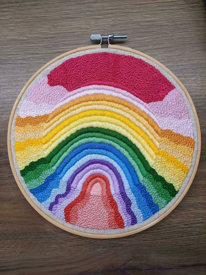 Colorful rainbow embroidery design in wooden hoop on wood surface showcasing beautiful embroidery patterns.