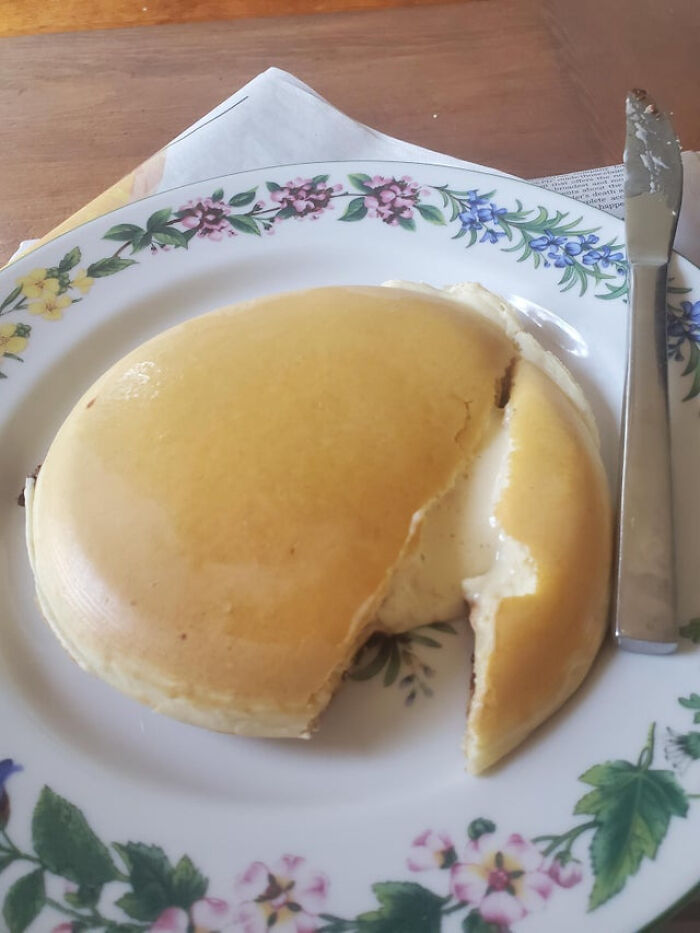 A pancake split with a slice of cheese inside on a floral plate, showcasing unusual dish creativity.