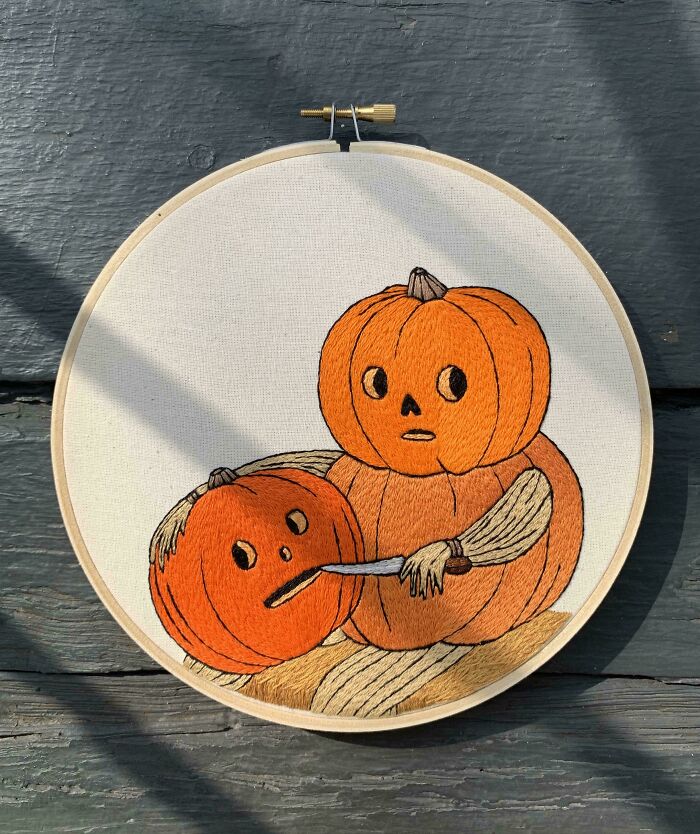 Embroidery hoop art featuring two expressive pumpkins, one carving the other, showcasing beautiful embroidery designs.