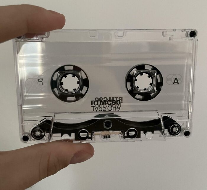 A person's hand holding a vintage cassette tape, illustrating regretful money spending decisions.