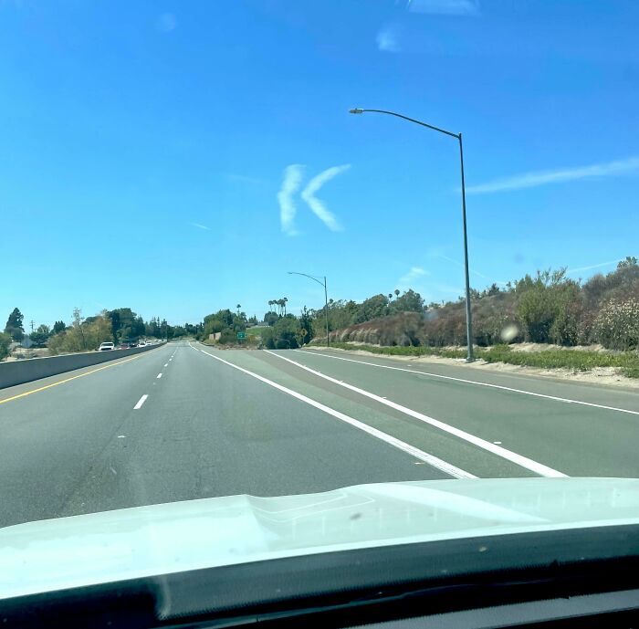 Unusual cloud shapes resembling arrows in a clear sky above a highway.